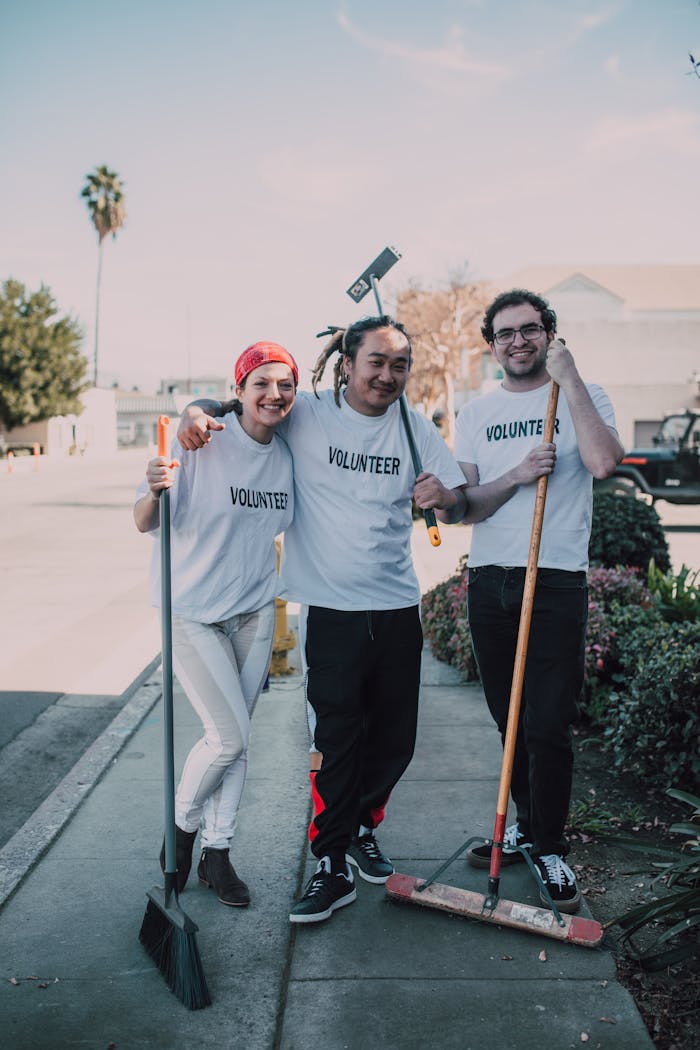 Happy volunteers in white shirts clean a neighborhood street, promoting community service.